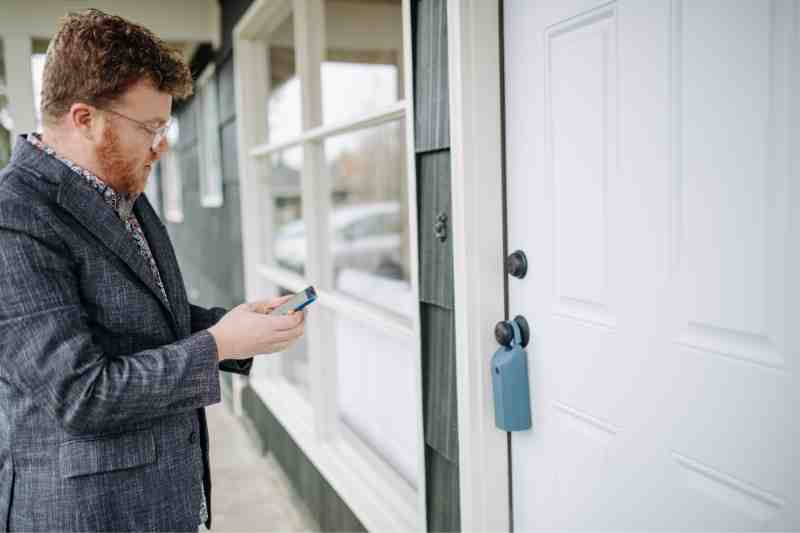 Man using smartphone to unlock smart lock on white door.