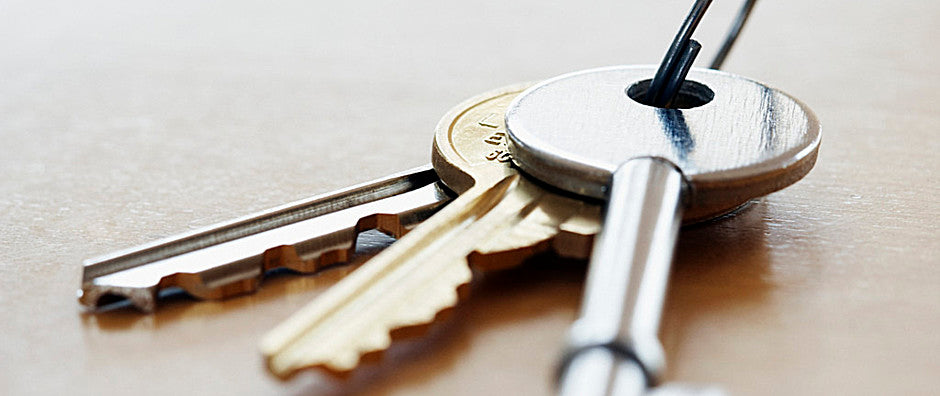 Silver and gold house keys on a light wood surface.